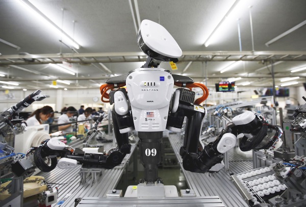 A humanoid robot works side by side with employees in the assembly line at a factory of Glory Ltd., a manufacturer of automatic change dispensers, in Kazo, north of Tokyo, Japan, in this July 1, 2015 file photo. Glory is in the vanguard as Japanese firms ramp up spending on robotics and automation, responding at last to premier Shinzo Abe's efforts to stimulate the economy and end two decades of stagnation and deflation.   REUTERS/Issei Kato/Files